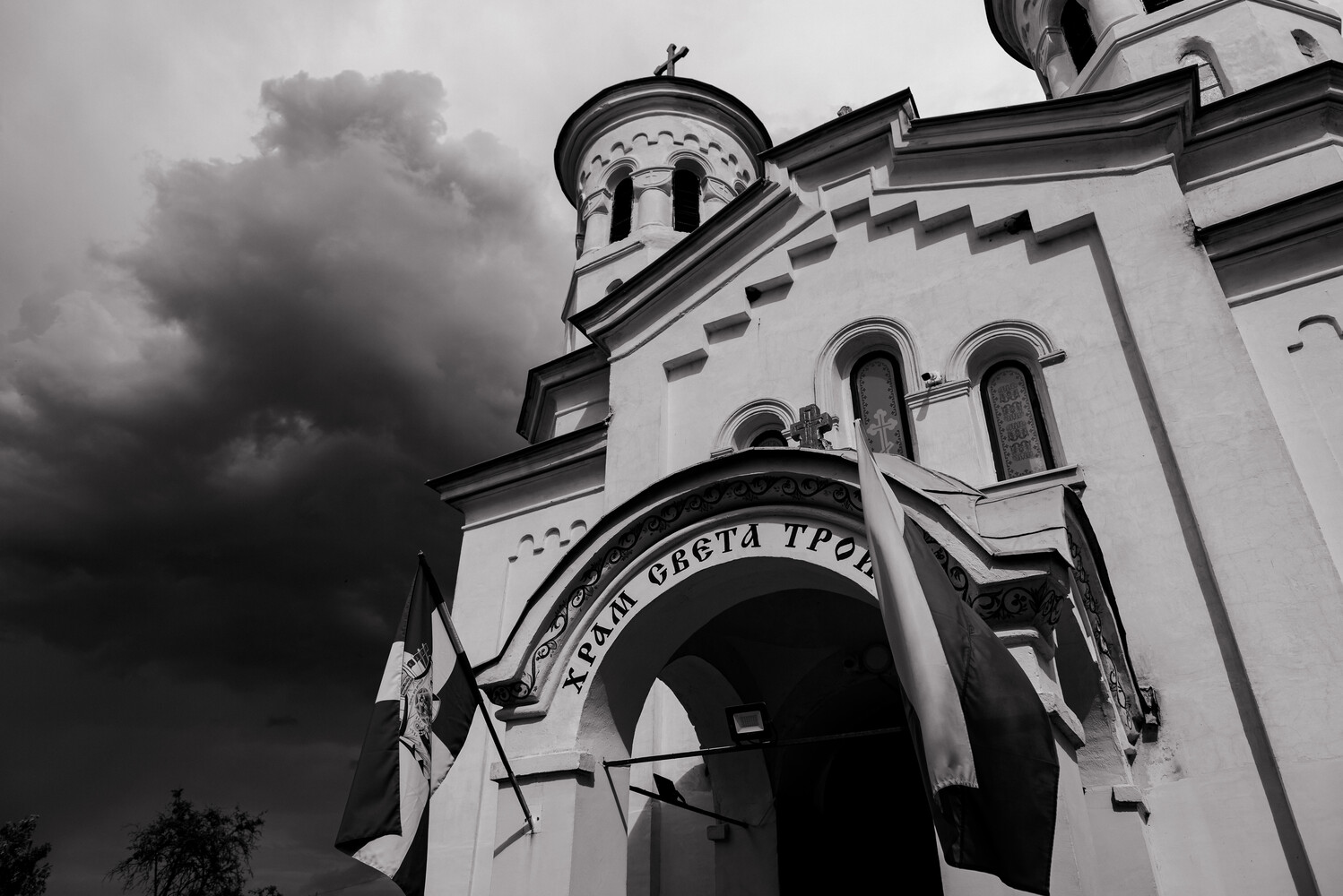 White Orthodox church with ornate dome and cross under dramatic storm clouds