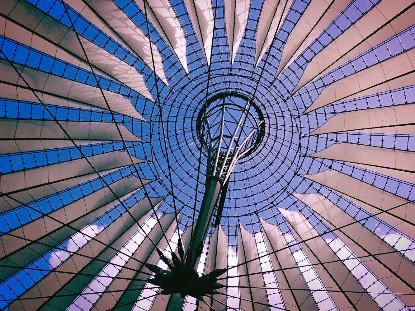 Upward view through a geometric glass dome structure with radial panels in blue and pink tones