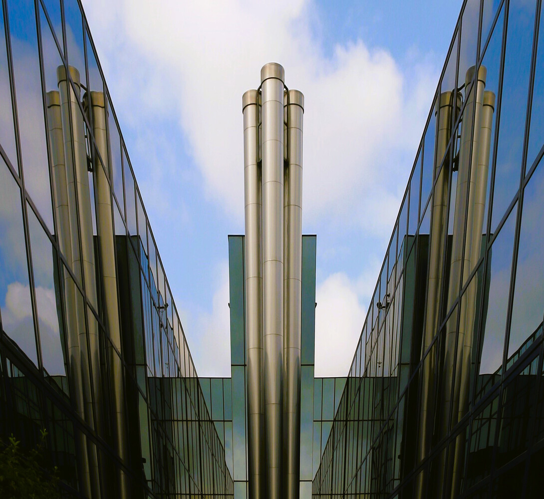 Symmetrical architectural composition of mirrored glass and steel buildings flanking a central metal tower