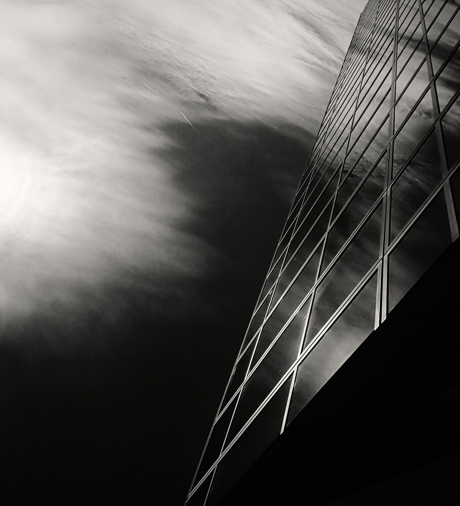 Modern building facade with geometric cable lines against dramatic cloudy sky in black and white