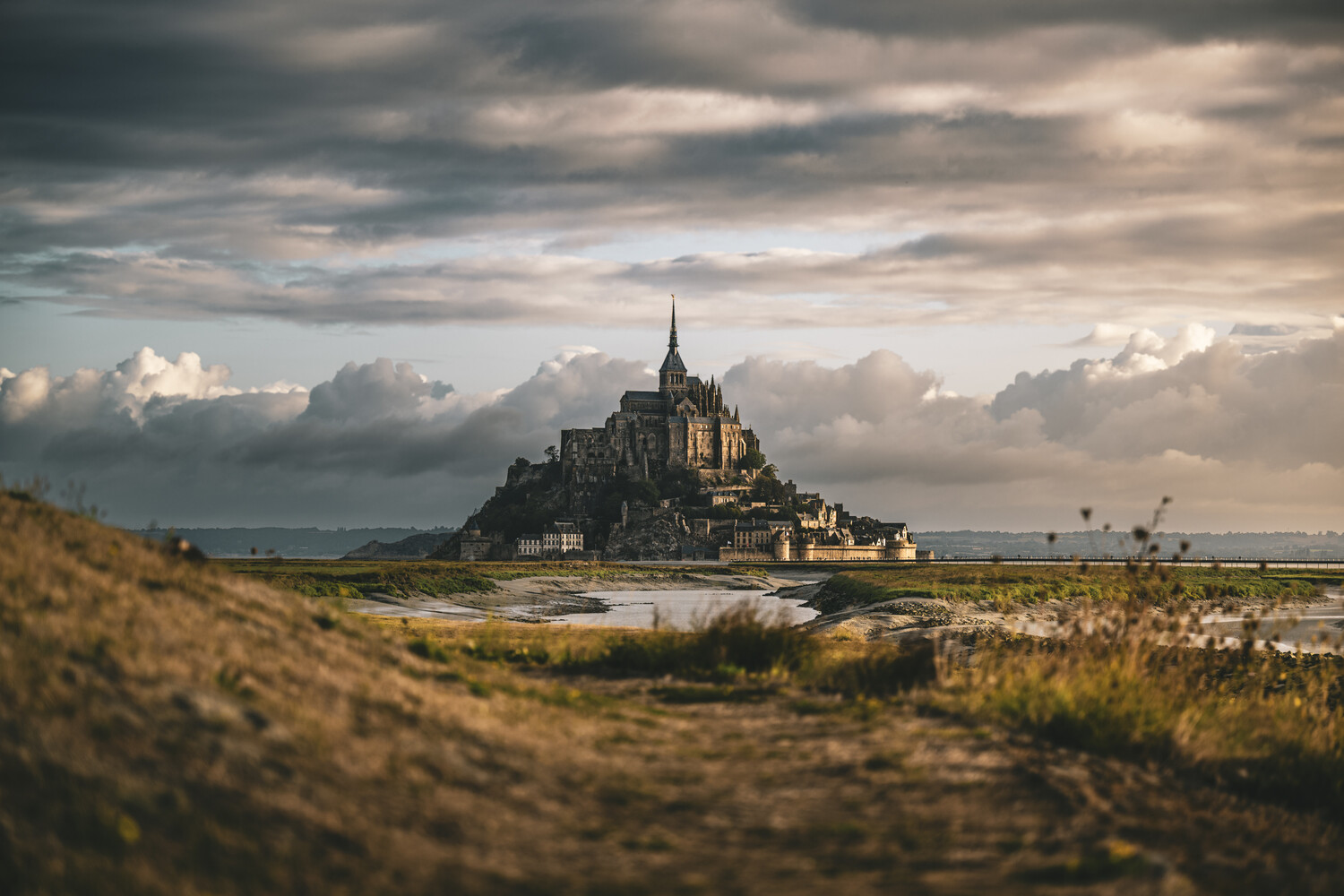 Medieval castle on tidal island surrounded by mudflats under dramatic cloudy sky