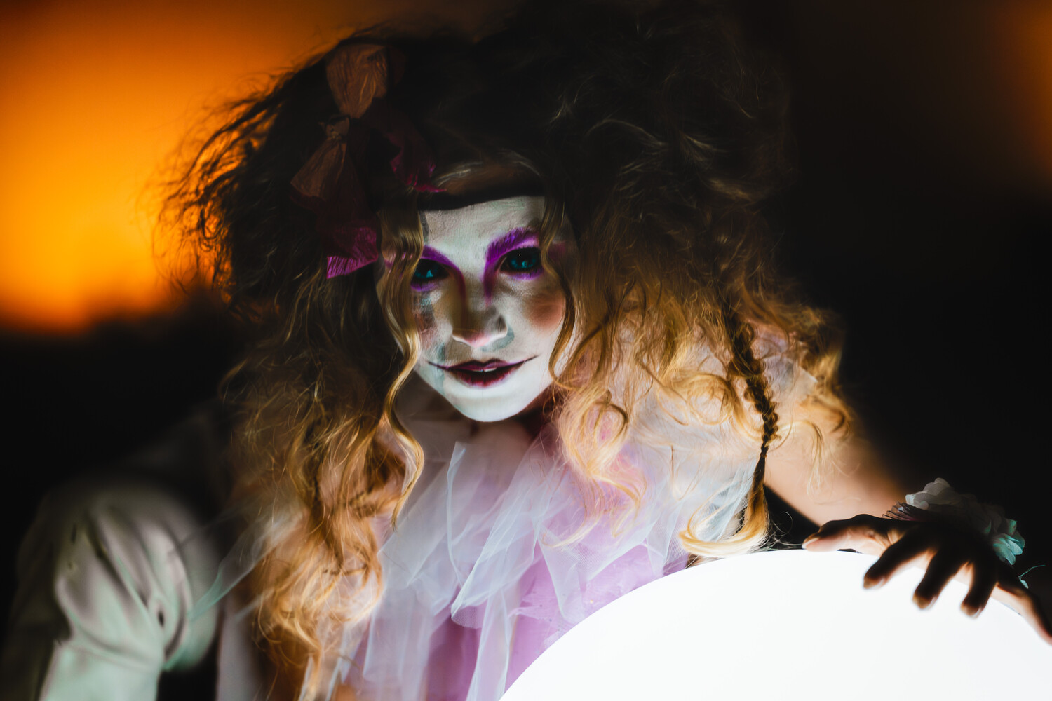 Person with white and purple face paint and curled blonde hair illuminated by warm golden light