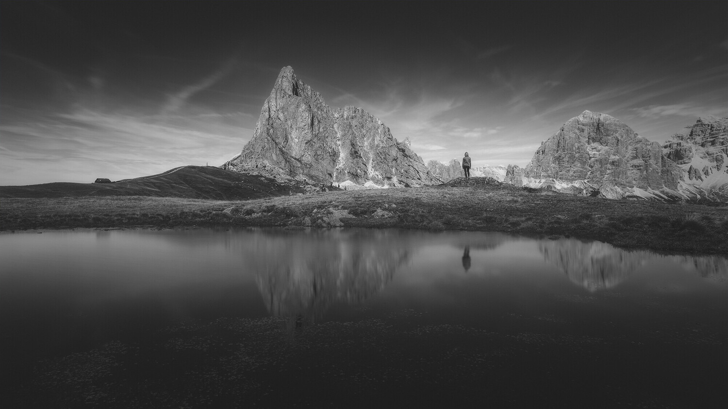 Dramatic rocky peaks reflected in still water under moody sky with solitary figure