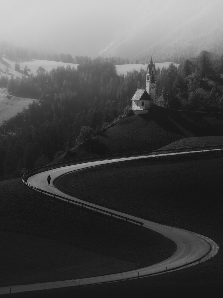 Church with white steeple nestled in forested valley with winding road in black and white