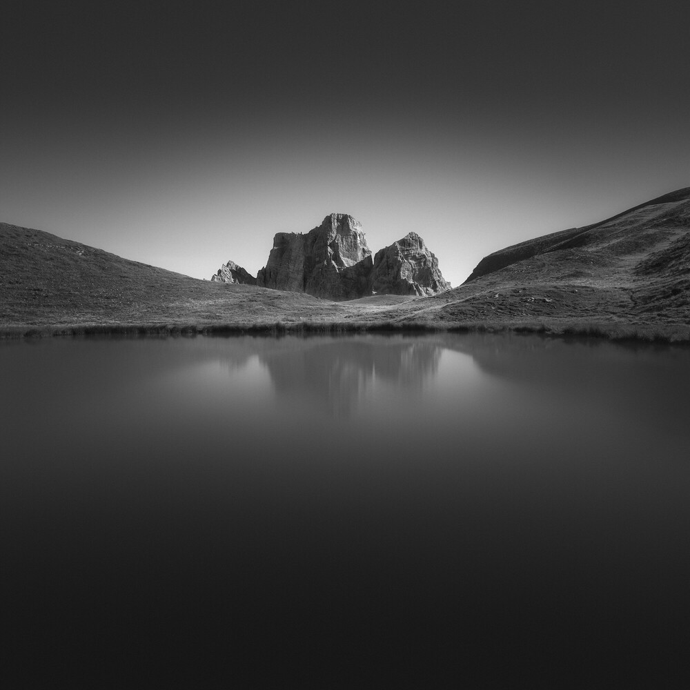 Rocky mountain peak reflected in still lake surrounded by barren hillsides