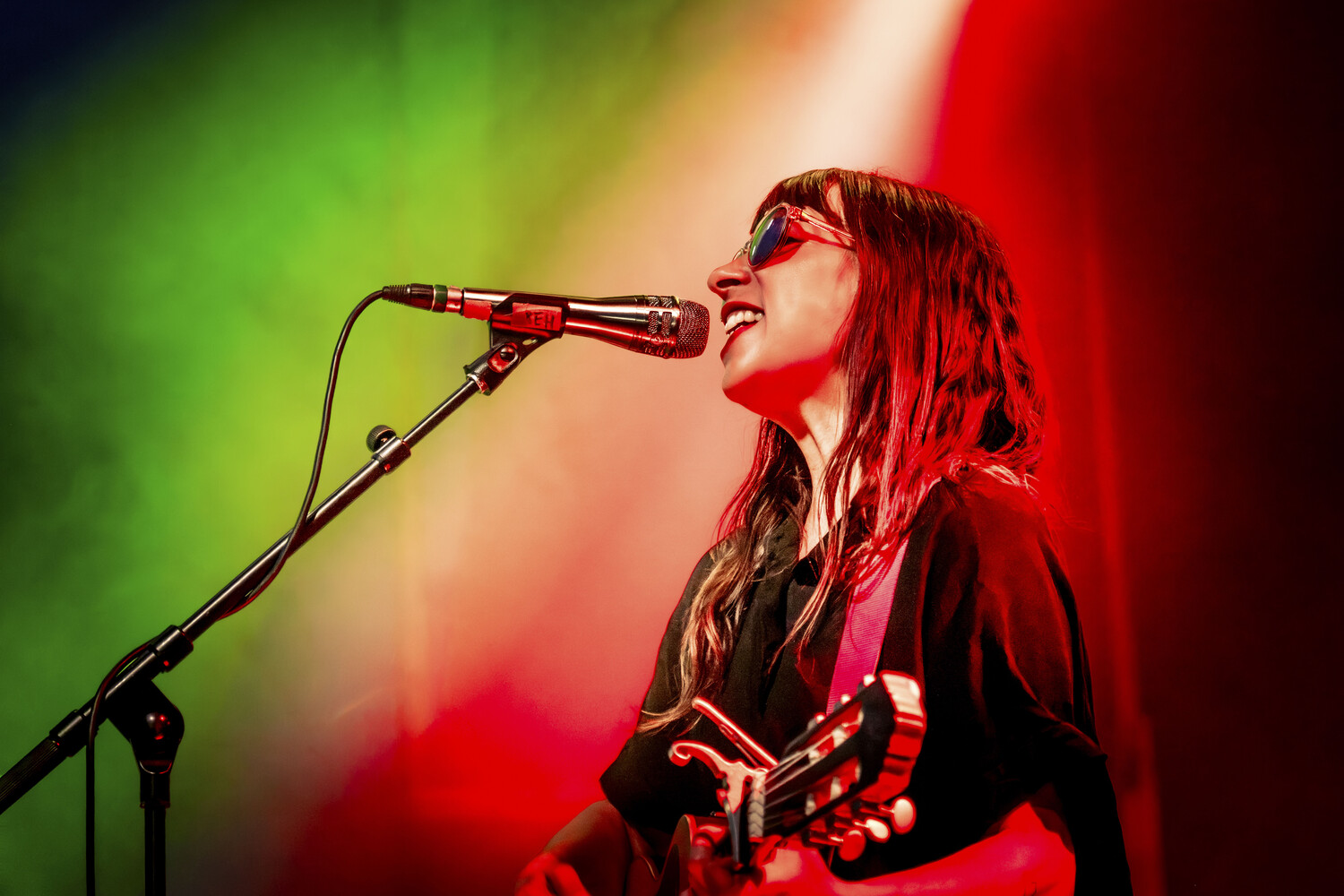 Female vocalist singing into microphone with electric guitar against colorful stage lighting