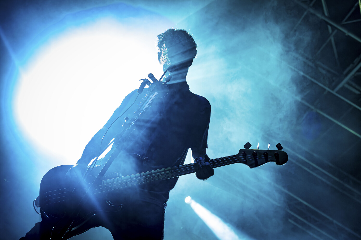 Silhouetted musician holding electric guitar against bright backlit stage lighting