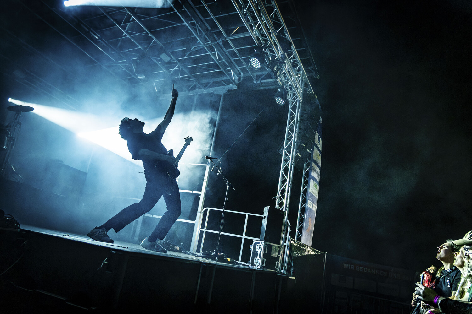 Performer mid-leap on concert stage with dramatic blue backlighting and metal truss framework