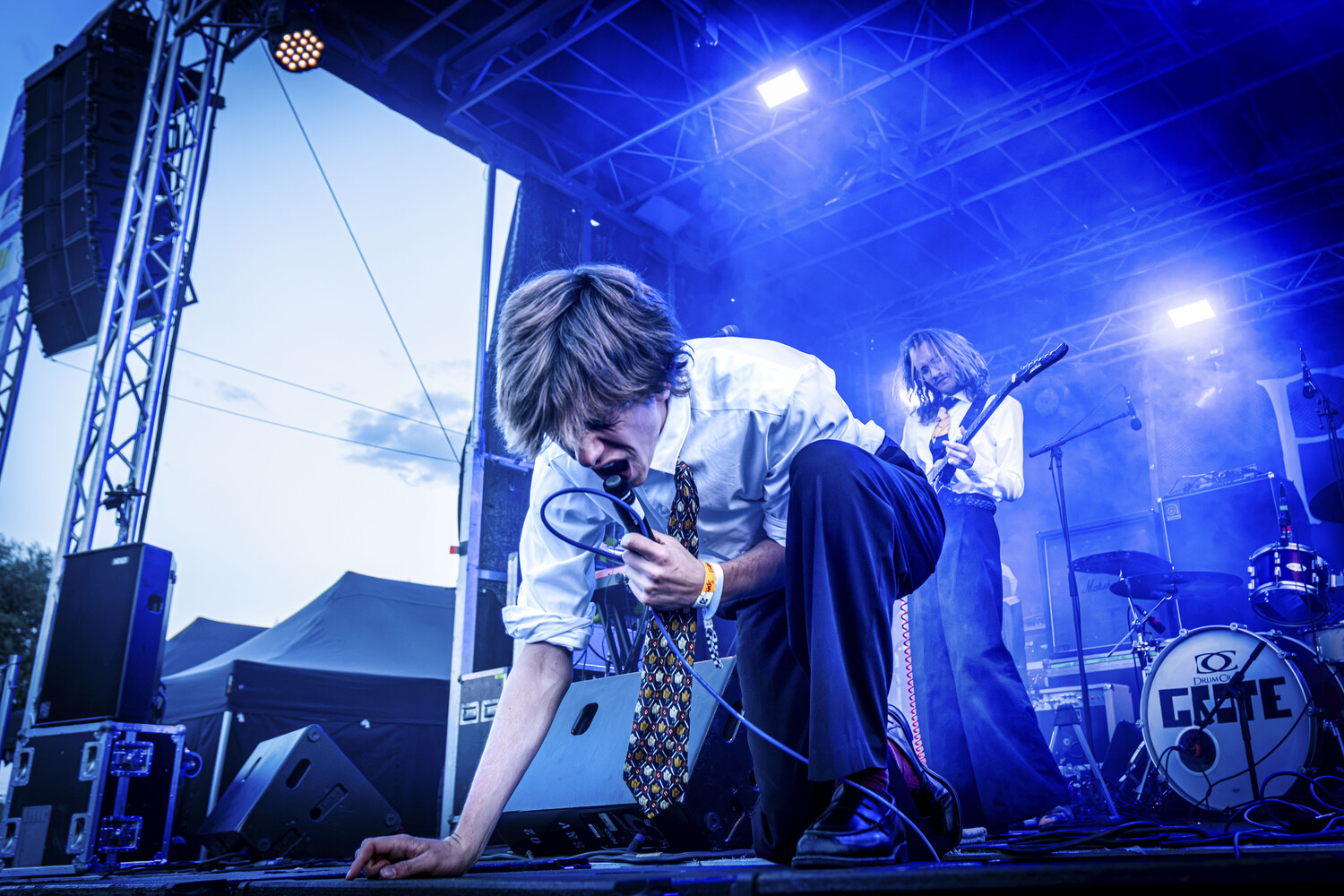 Musician performing on stage with guitar under blue stage lighting and truss rig