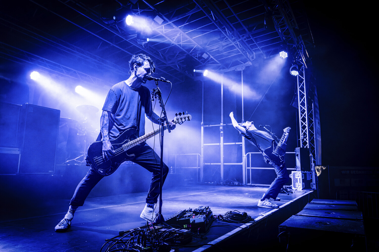 Guitarist performing on stage with blue spotlight lighting and bassist in background