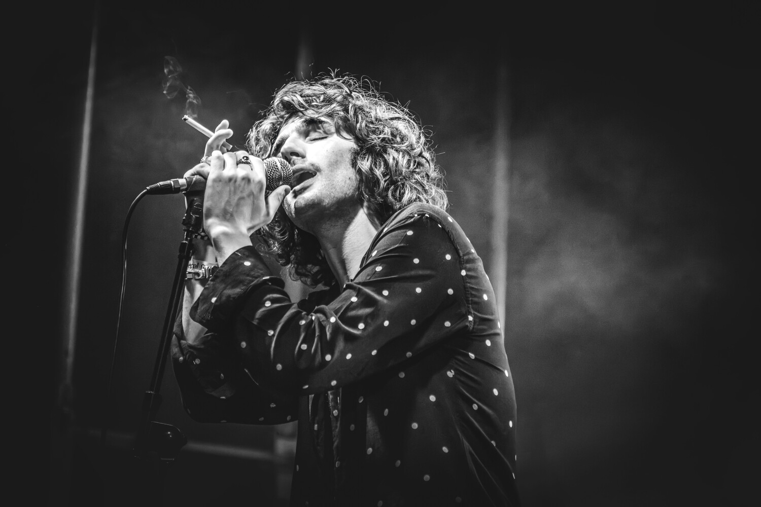 Black and white photograph of a performer singing passionately into a microphone, wearing a studded jacket