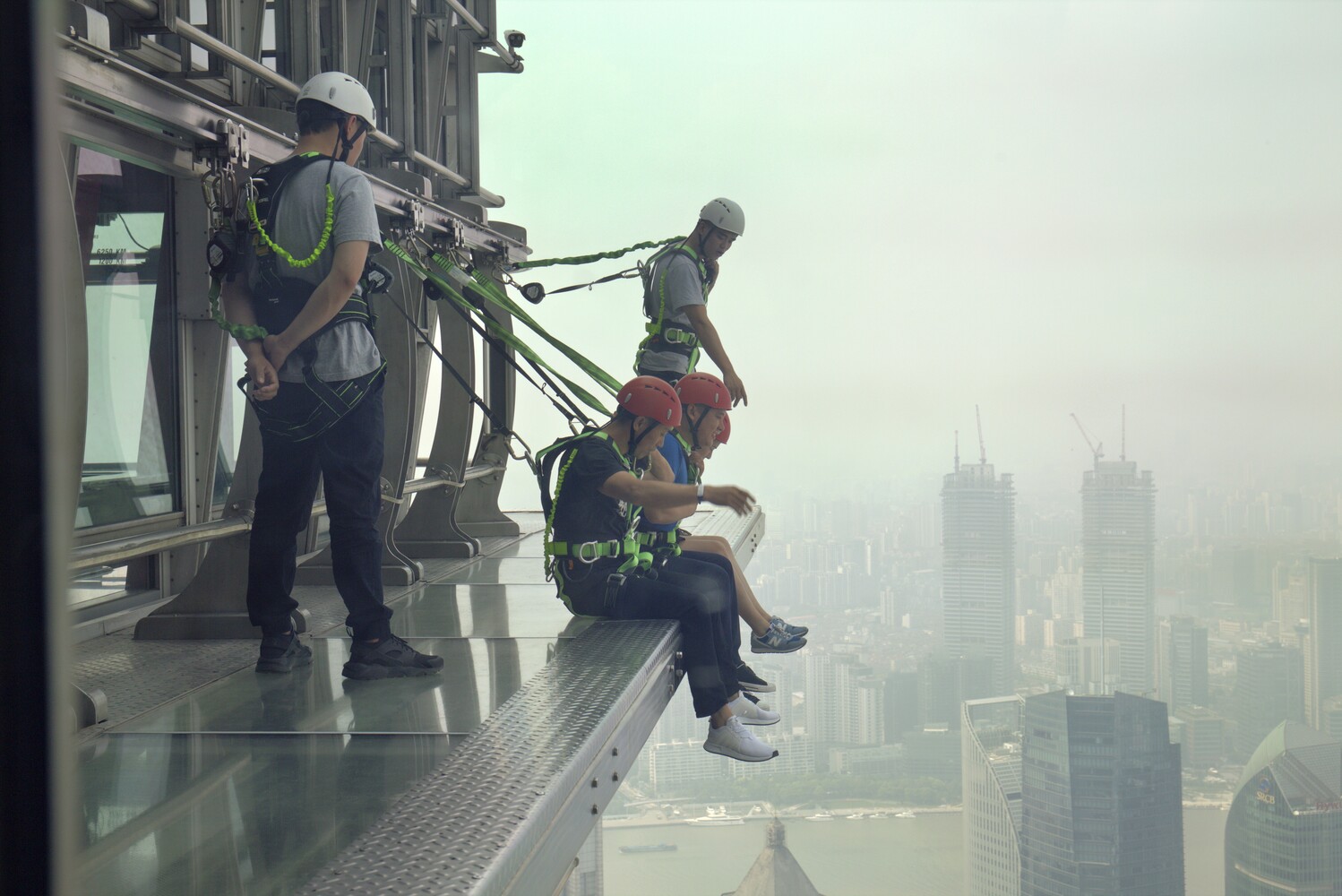 Three workers on high-rise building ledge with safety equipment overlooking misty cityscape