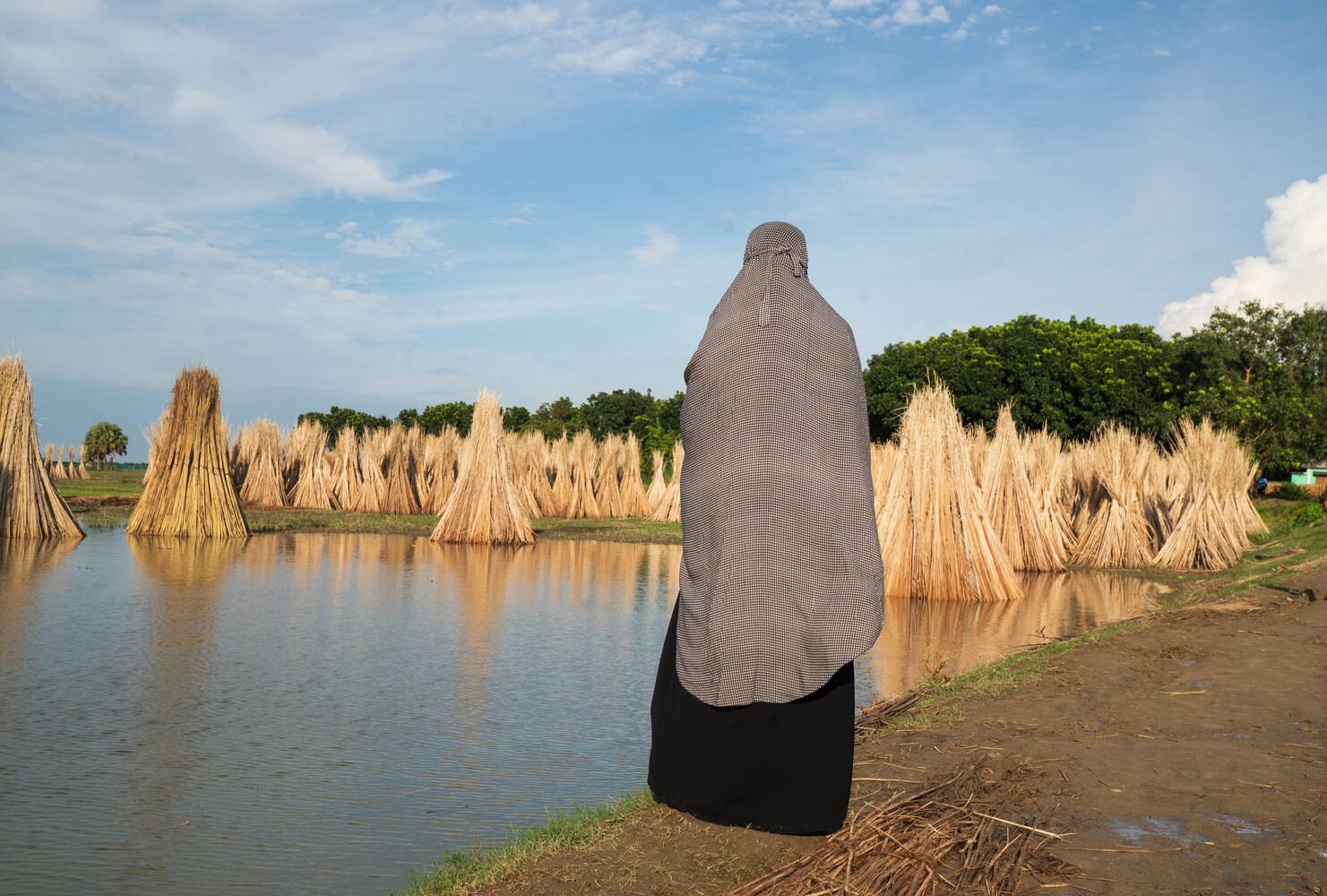 Person in gray and black clothing standing by reed-lined waterway