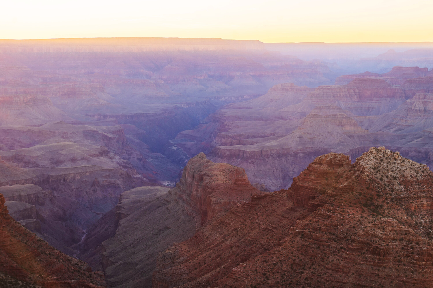 Grand Canyon landscape at sunrise with layered rock formations and Colorado River visible in misty valley
