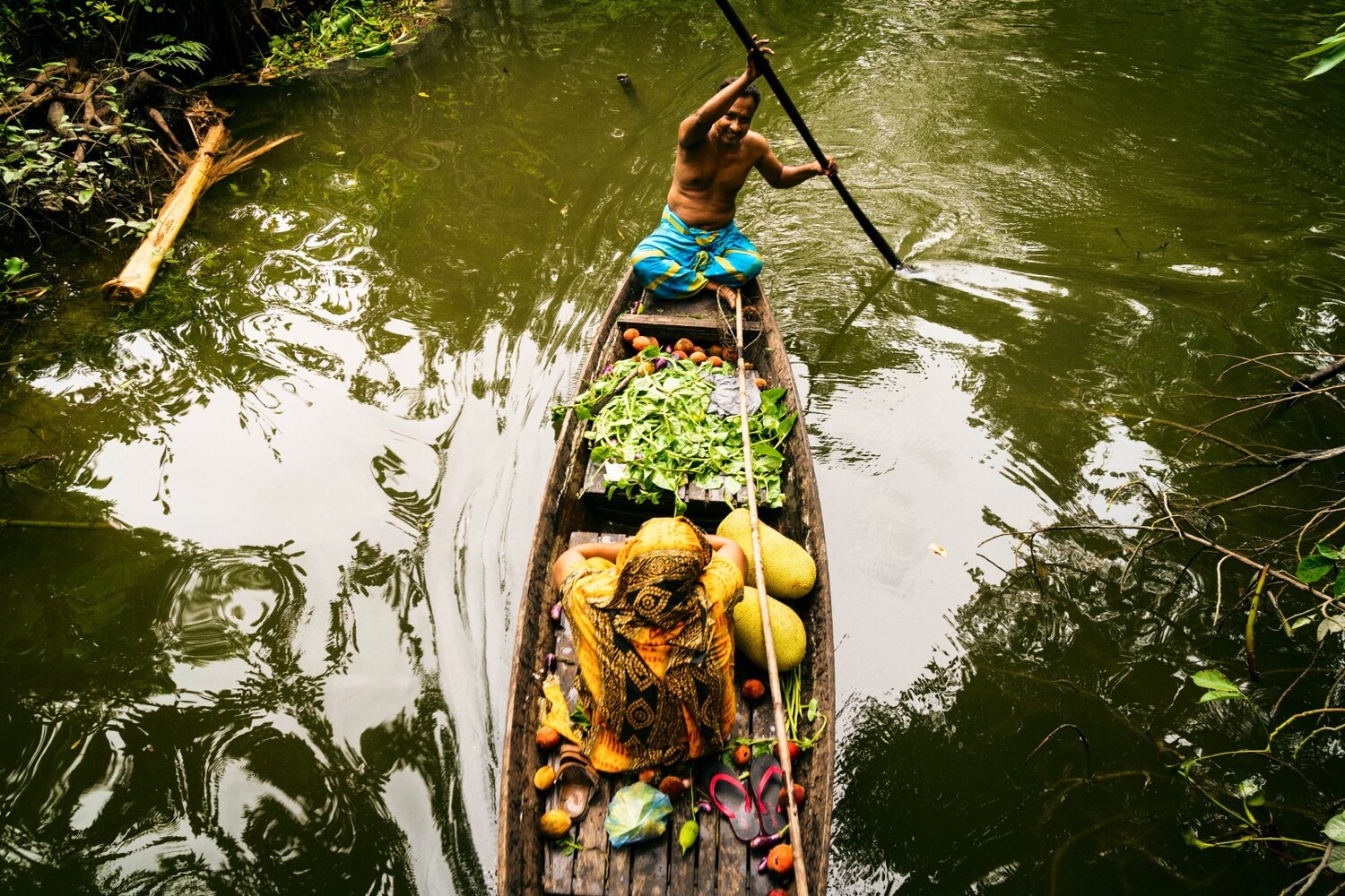 Overhead view of a wooden boat loaded with fresh tropical produce on a green waterway
