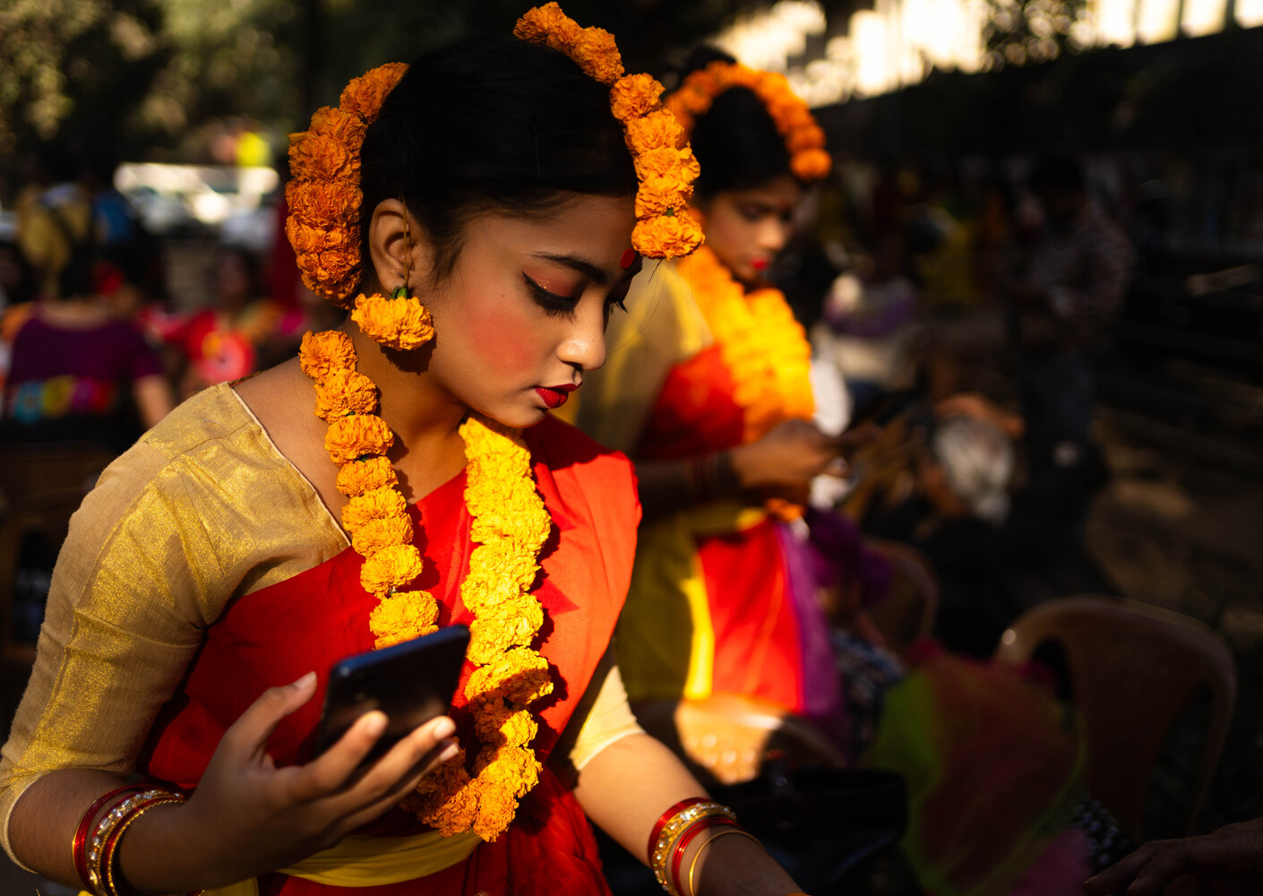 Woman wearing yellow and red clothing adorned with bright orange marigold garlands at a festive outdoor celebration