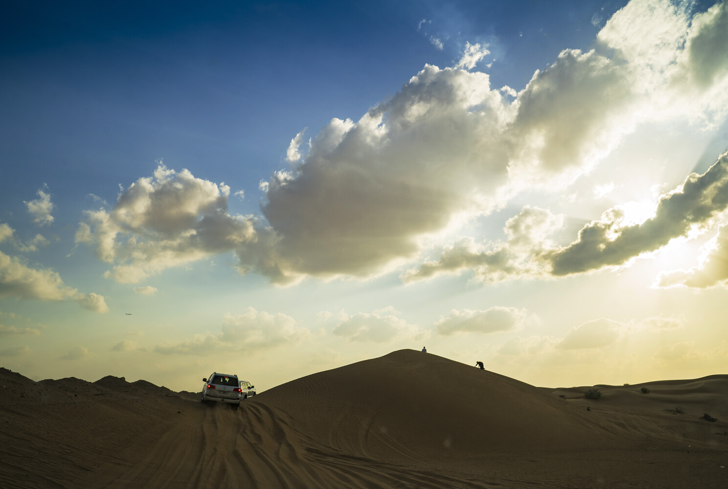 Off-road vehicle driving across desert sand dunes under dramatic cloudy sky