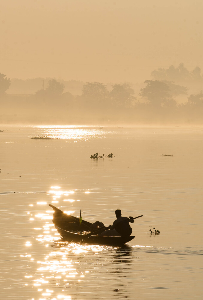 Fisherman in wooden boat on misty water at sunrise with golden light reflections