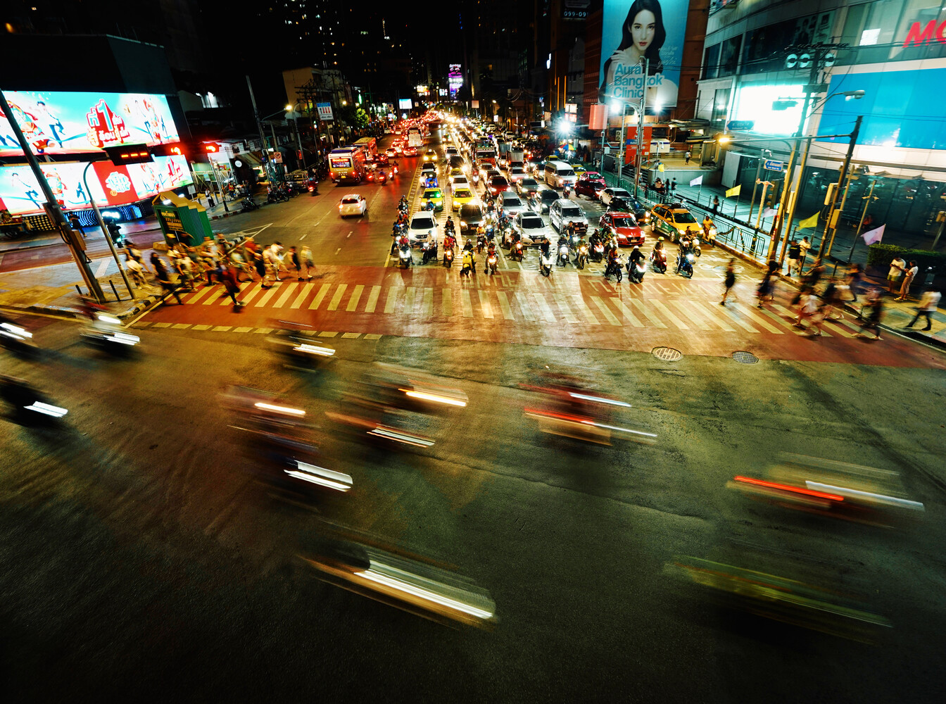 Busy urban intersection at night with motion blur from traffic and pedestrians crossing