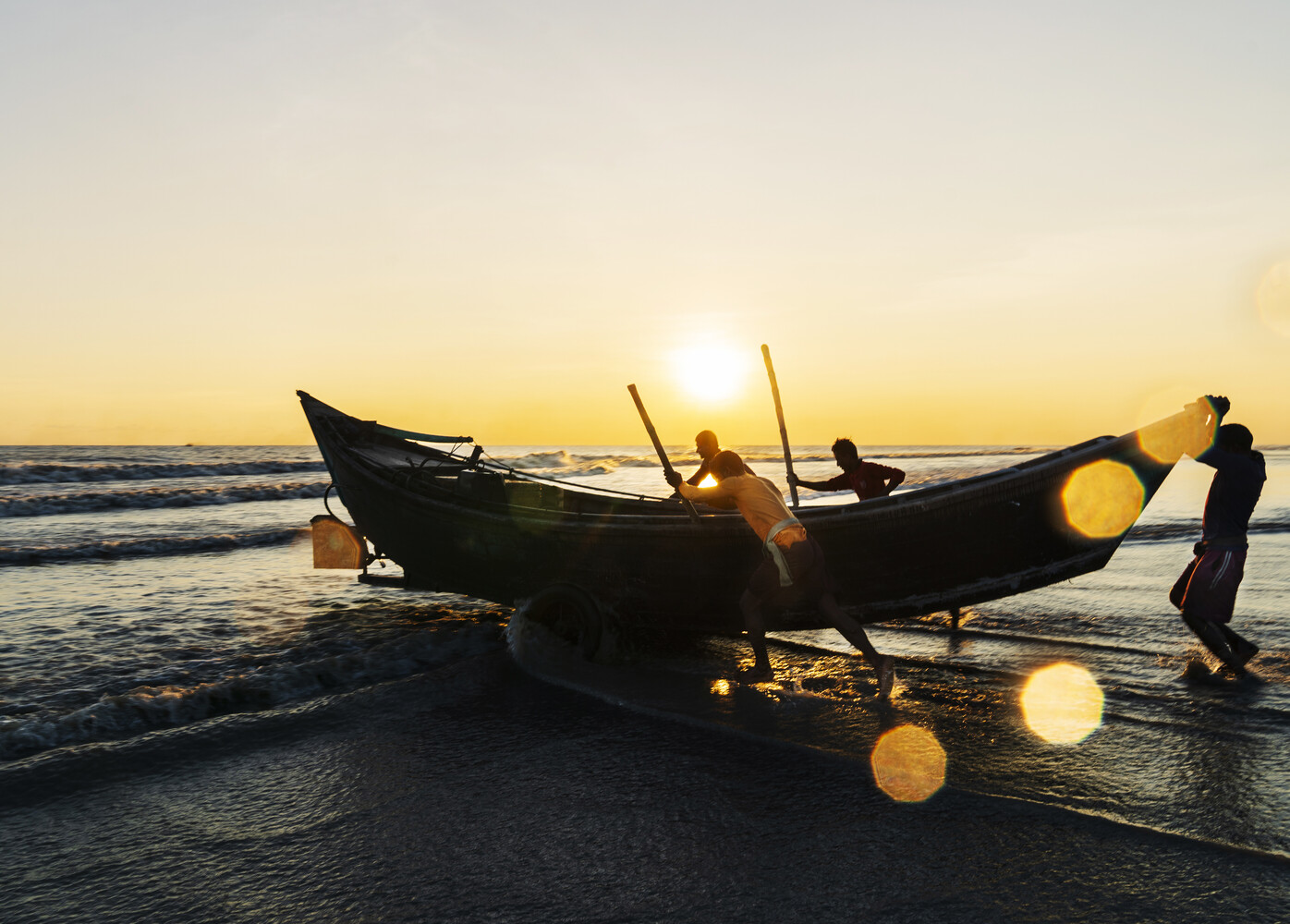 Silhouetted fishermen positioning wooden boats at the shore during golden hour sunrise