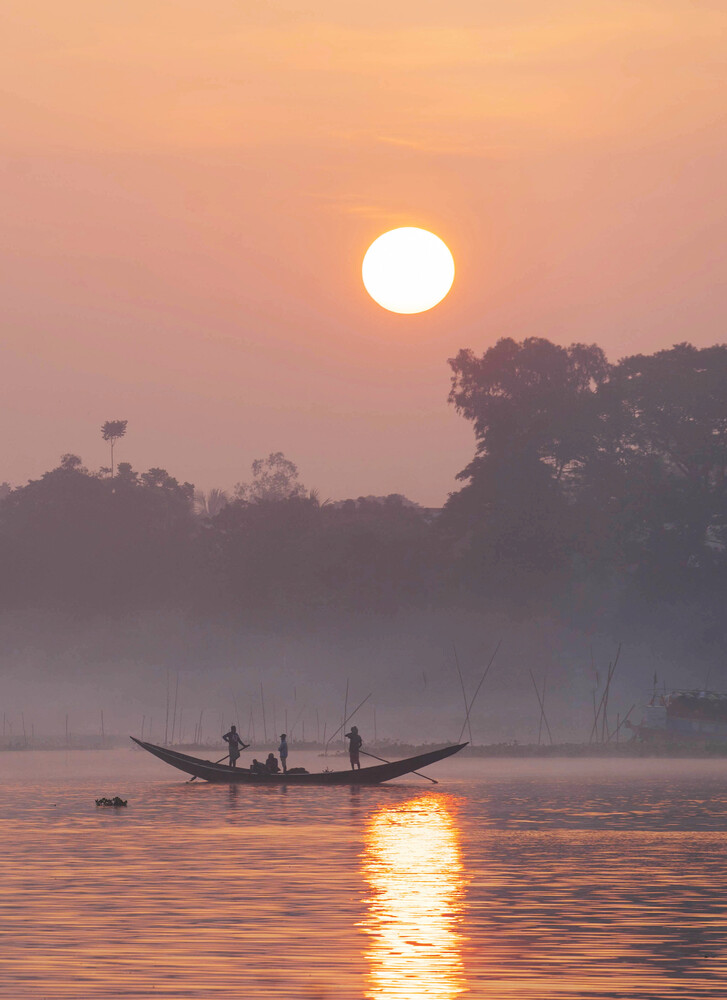 Wooden boat with silhouetted figures on misty river at sunrise