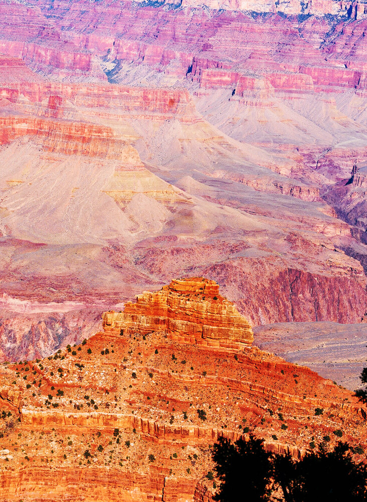 Sunlit red sandstone butte in the foreground with layered canyon walls fading into pink and purple haze in the distance