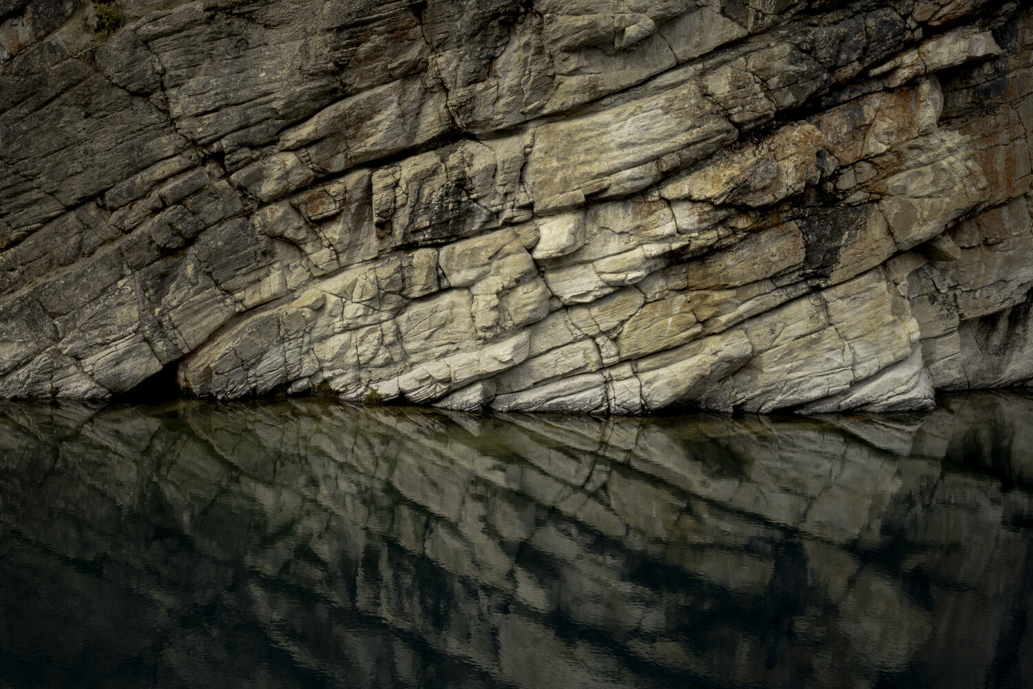 Layered rock formation reflected in still water below