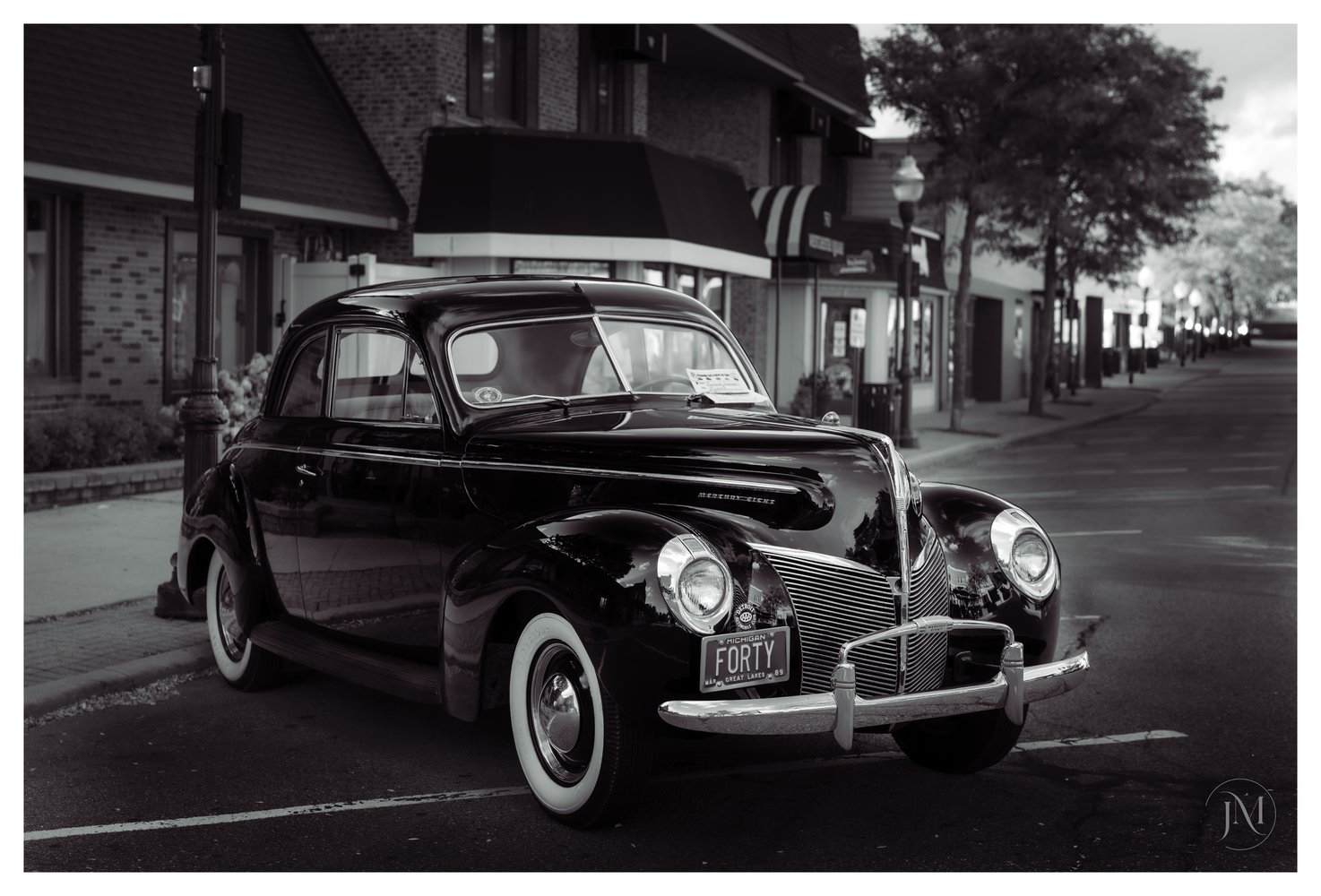 Black vintage car with white-wall tires parked on a tree-lined residential street