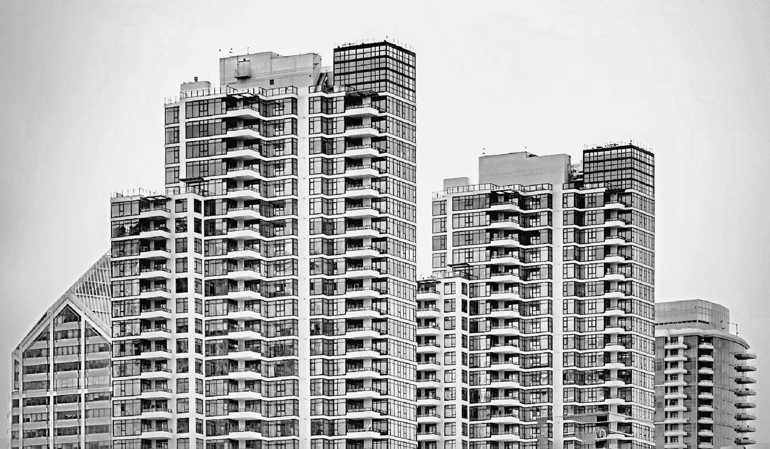 Black and white view of several high-rise residential towers with rows of balconies and grid-patterned glass facades against an overcast sky.