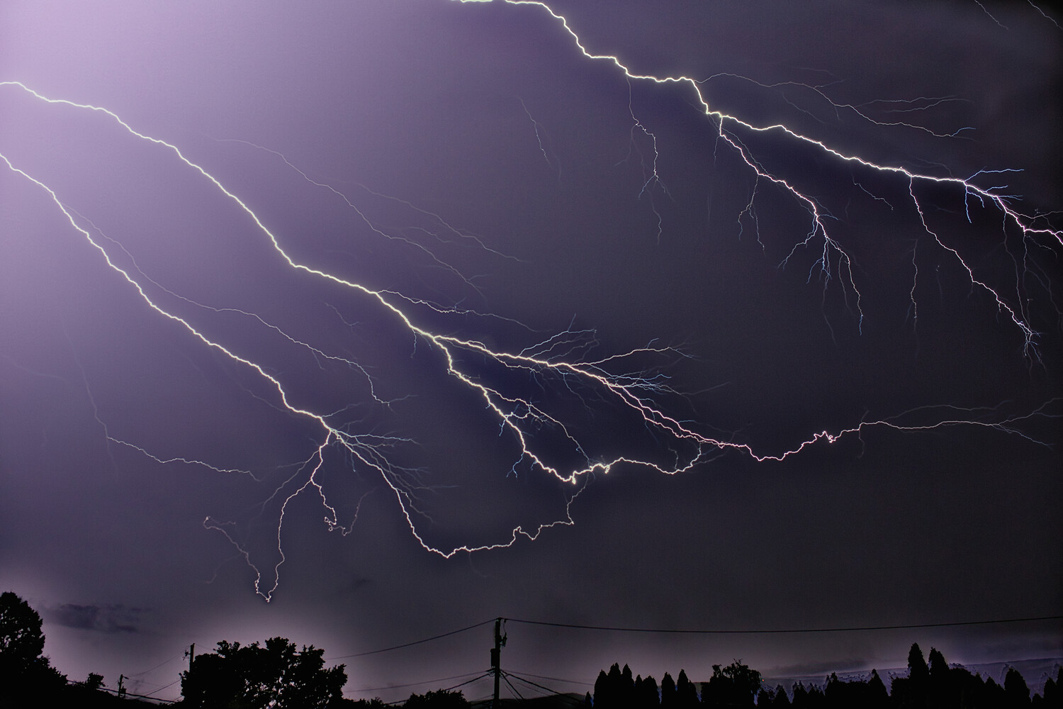 Branching lightning bolts illuminate a dark purple storm sky above a silhouetted landscape