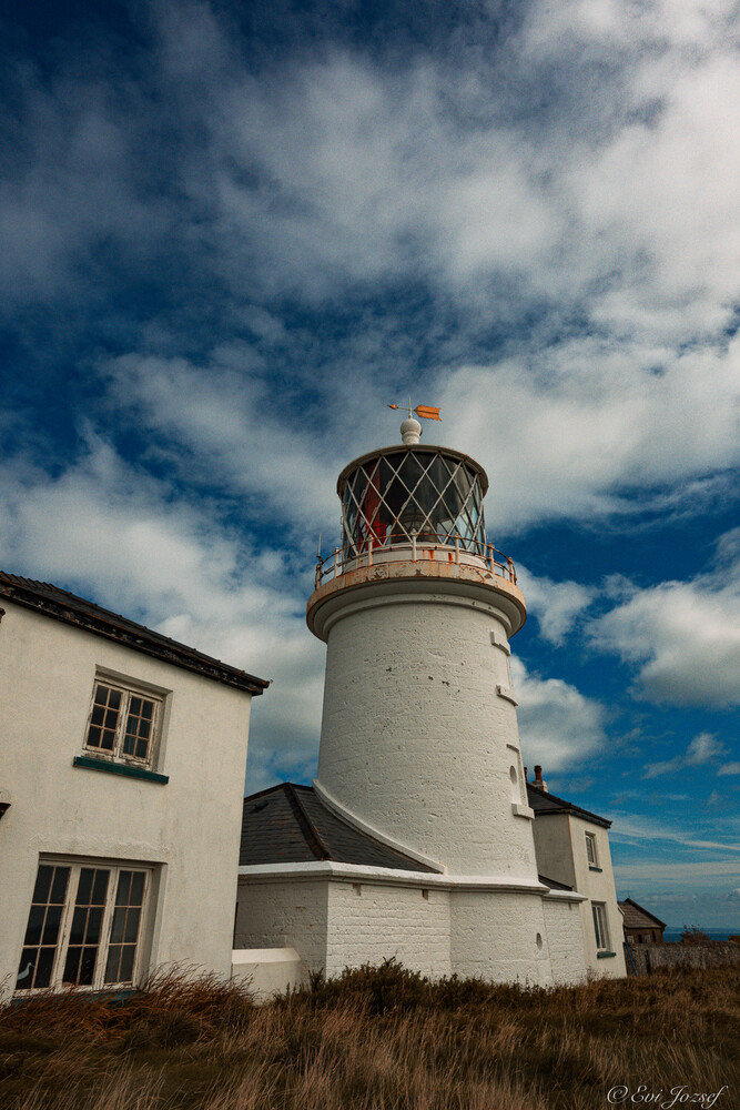 White lighthouse with ornate red and gold lantern room against dramatic blue cloudy sky
