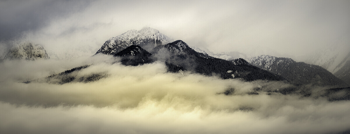Snow-capped mountain peaks emerging from dense low-lying clouds and mist