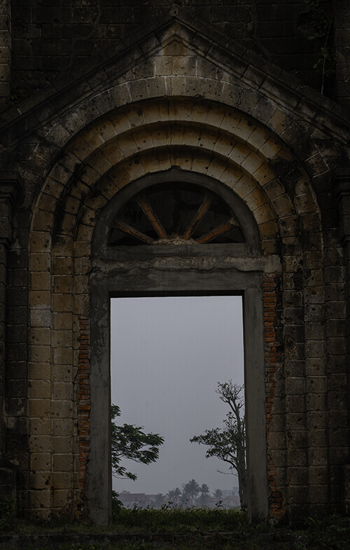 Stone archway framing a foggy, overcast sky and two bare trees through a tall doorway in an old ruined building.
