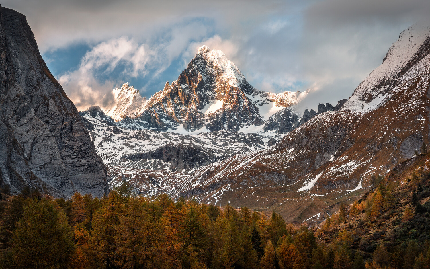 Snow-capped alpine peak framed by golden larch forests and rocky mountain ridges