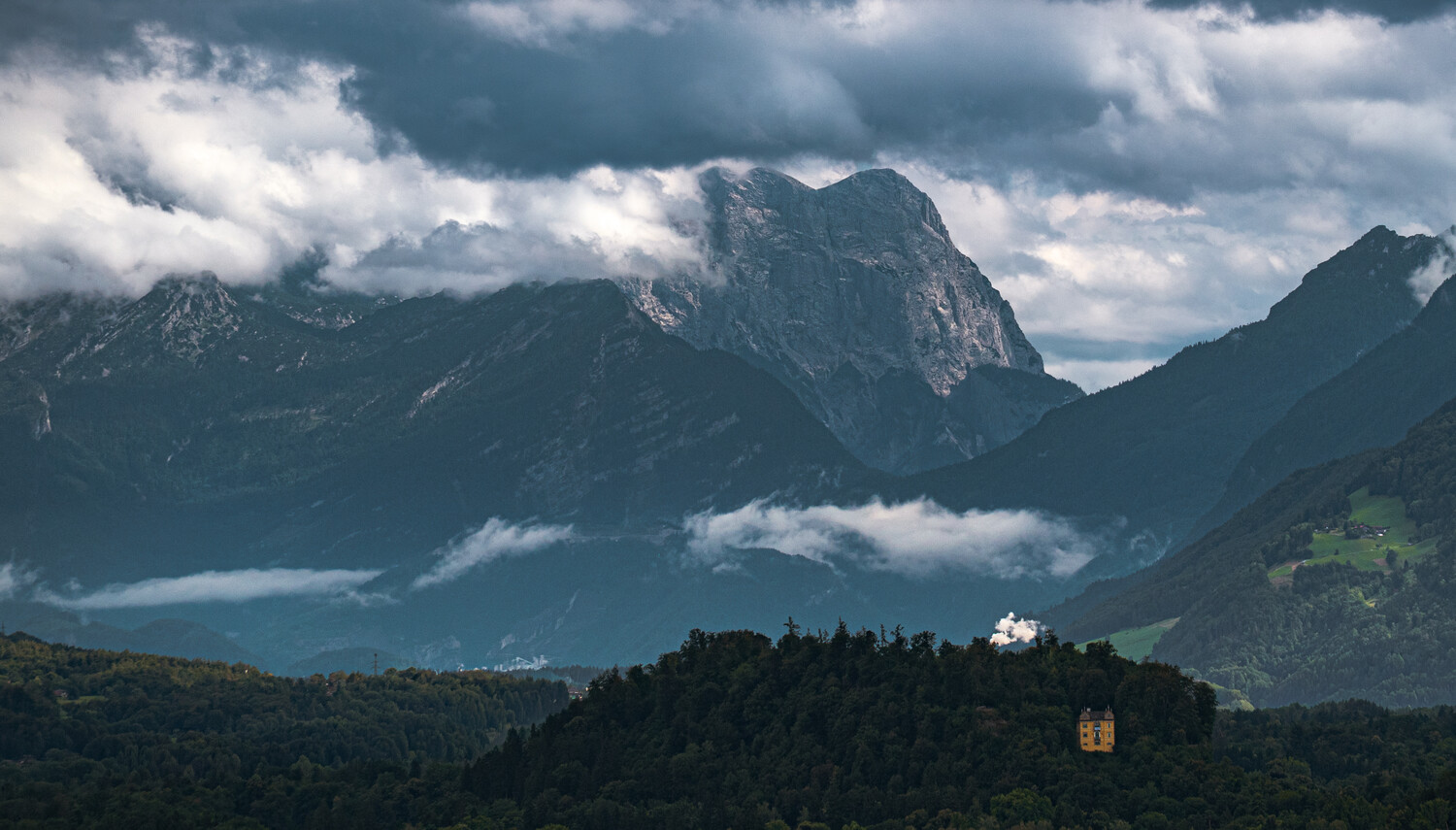 Alpine lake nestled between dramatic peaks with castle perched on forested hillside