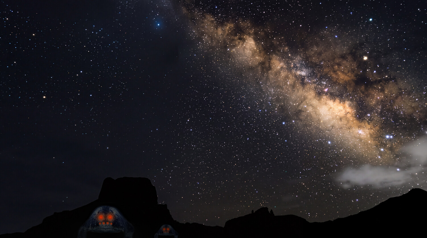Milky Way galaxy arching across night sky above silhouetted desert landscape with glowing tent