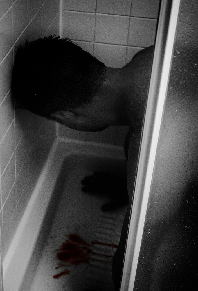 Black and white overhead view of person lying in bathtub with water and red liquid