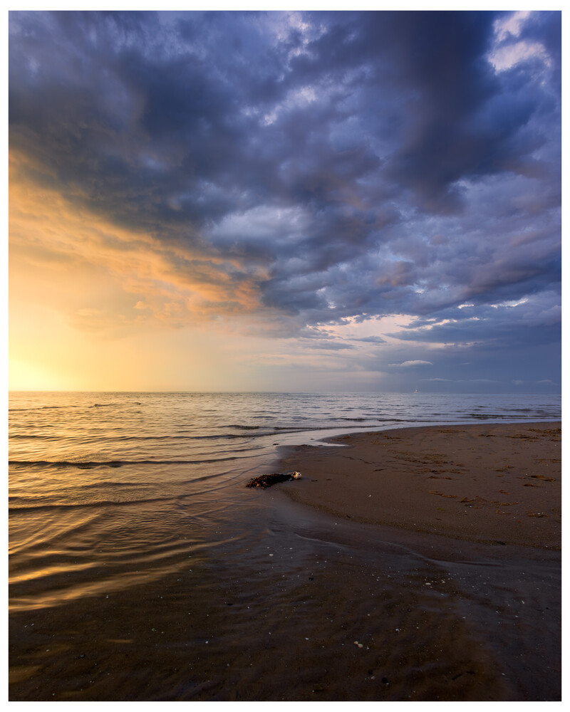 Dramatic coastal sunset with stormy clouds and golden light reflecting on wet sand