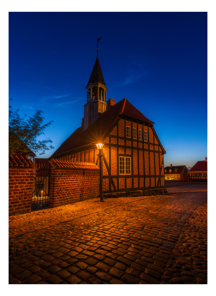 Half-timbered church with illuminated facade at dusk against deep blue sky