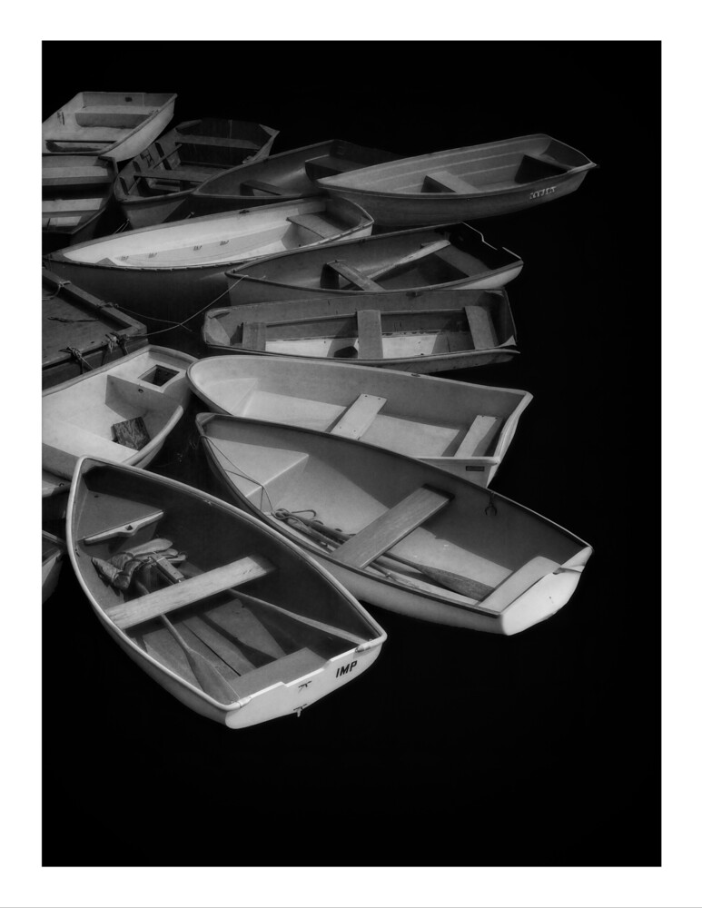 Multiple small rowboats arranged in overlapping rows against a black background in monochrome