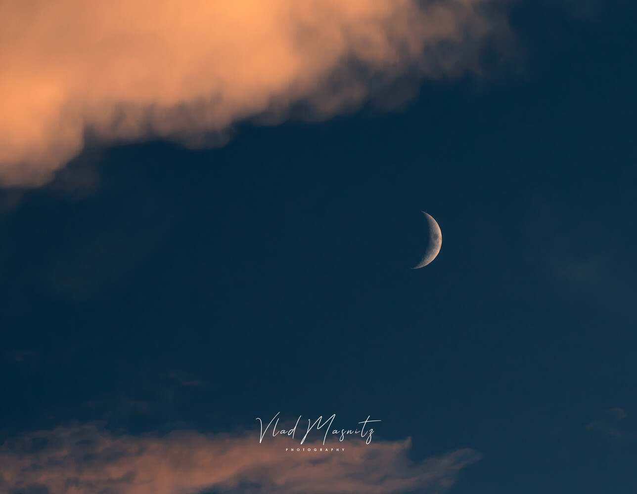 Crescent moon against deep blue twilight sky with golden cloud formations
