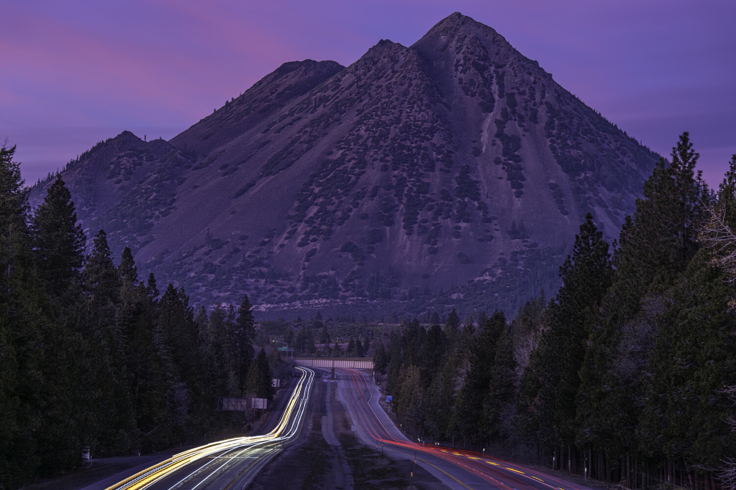 Long exposure photograph of a straight highway stretching toward a snow-covered mountain at twilight