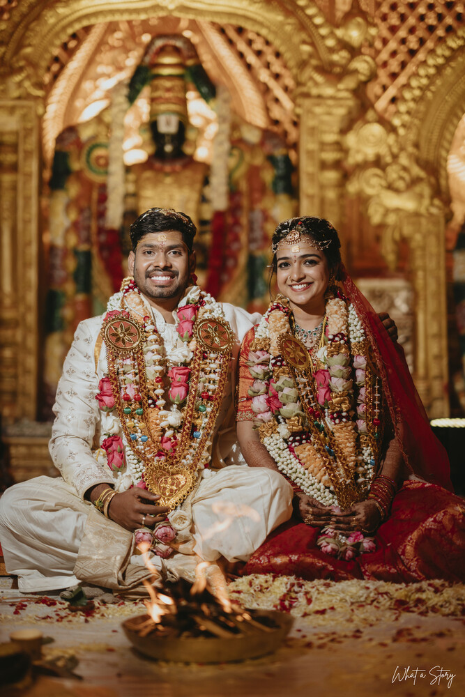 Bride and groom seated in floral garlands before a sacred fire during a South Indian wedding ceremony.