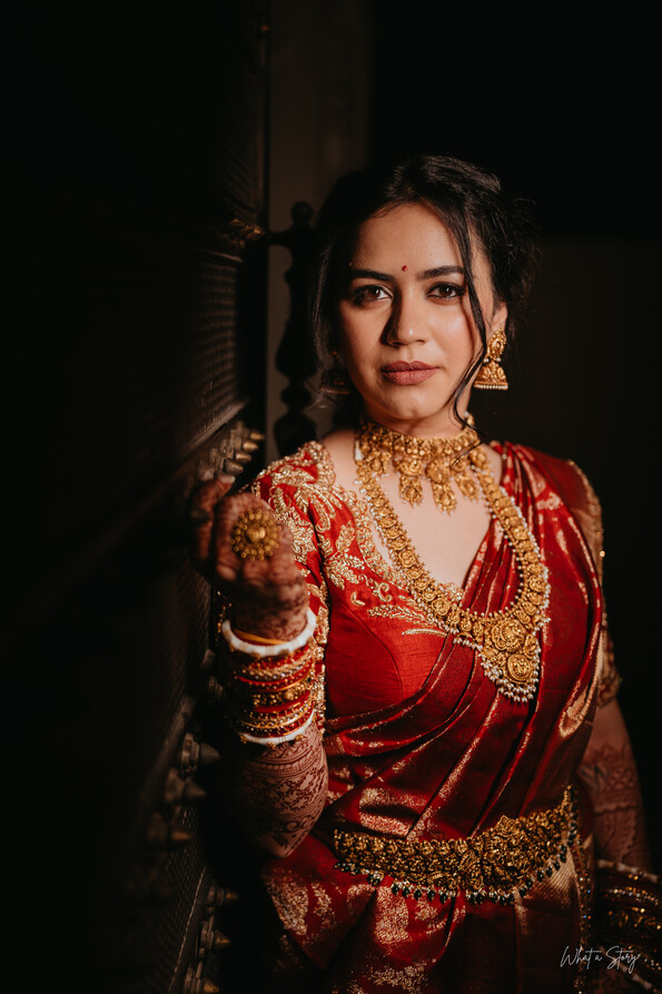 Portrait of a bride in red and gold traditional attire with heavy gold jewelry, posed against a dark background
