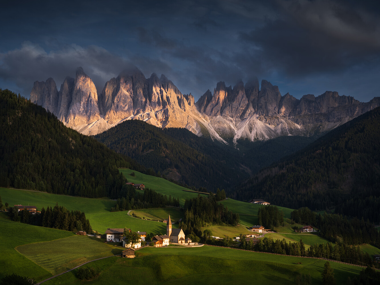 Alpine valley village nestled between forested slopes and dramatic jagged mountain peaks at golden hour