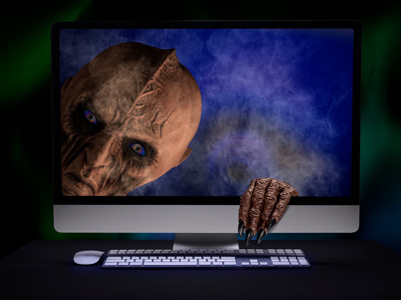 Monitor displaying a menacing alien creature face while a clawed hand reaches out from behind the screen onto the desk.