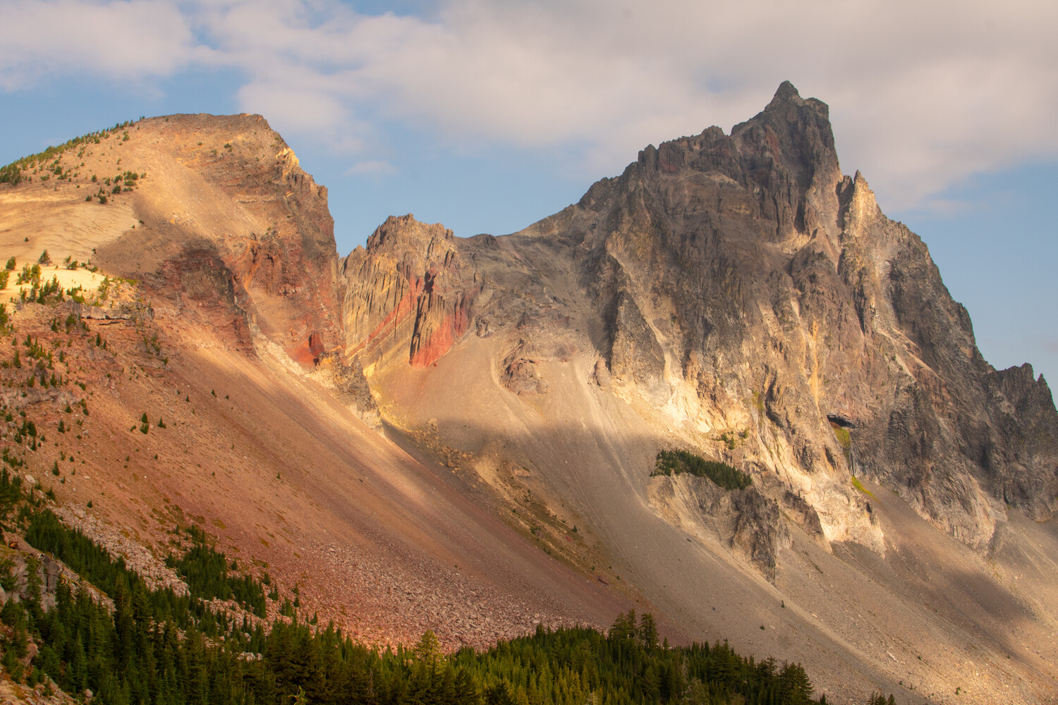 Jagged volcanic peaks with golden and gray rock formations rising above forested slopes