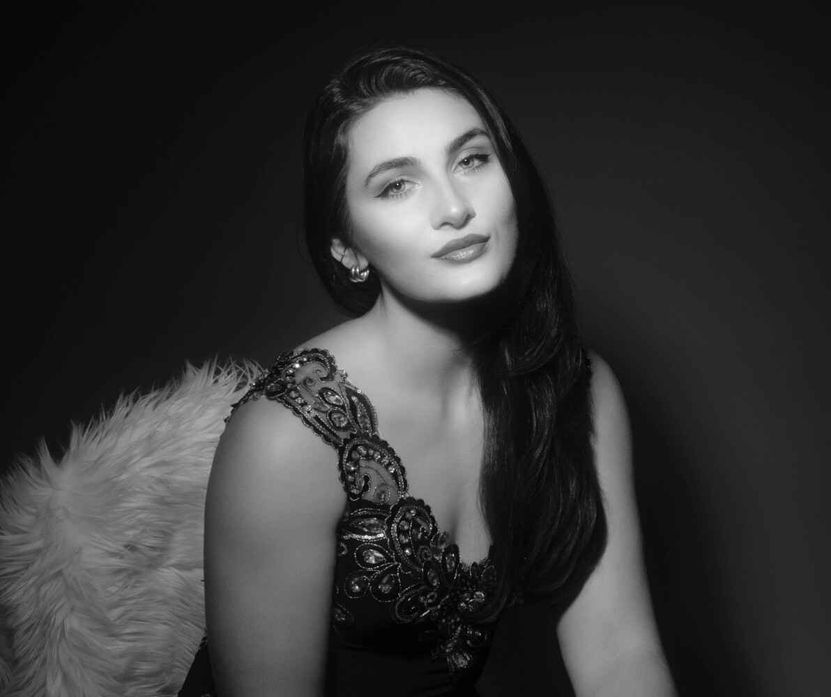 Woman with long dark hair in black and white studio portrait wearing embellished dress and fur stole