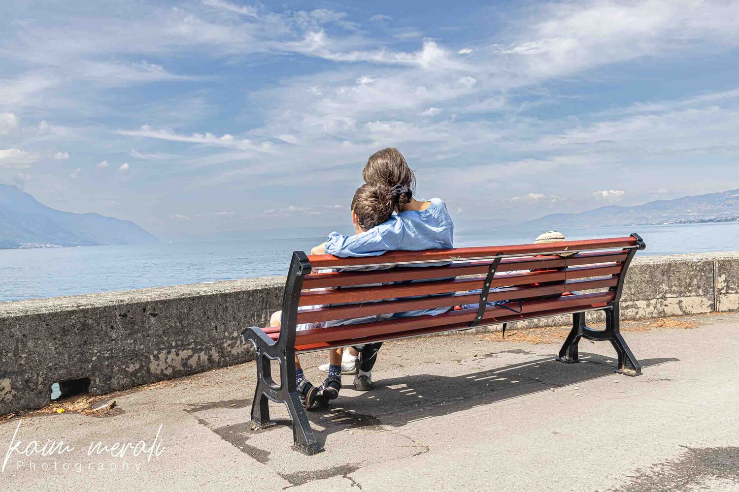 Woman with child sitting on wooden bench overlooking coastal landscape