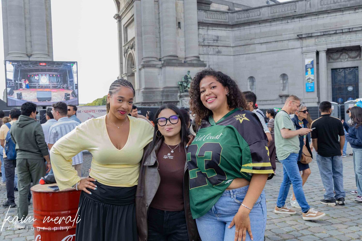 Three smiling women posing together at an outdoor urban event with historic architecture in background
